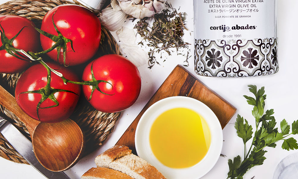 Cuenco con aceite de oliva virgen extra, tomates, ajo y botella de aceite Cortijo Abades, en plano cenital