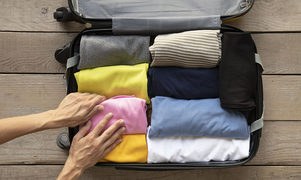 Maleta con ropa organizada en su interior y una mano añadiendo la última prenda