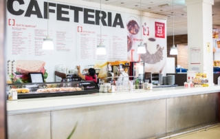 Barra de cafetería junto a personal trabajando y gran cartel al fondo en Mérida