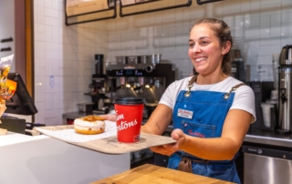 Camarera sonriendo ofreciendo café para llevar y un dulce en cafetería Tim Hortons