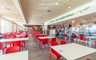 Mesas para comer junto al Self Service, en el lateral se aprecia la frase "Qué rico, sabor mediterráneo"