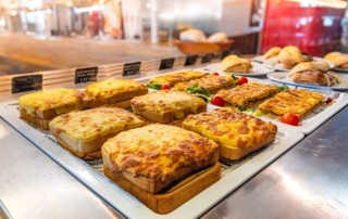 Bandejas con varios sandwich cubiertos de bechamel y trozos de empanada listas para comer