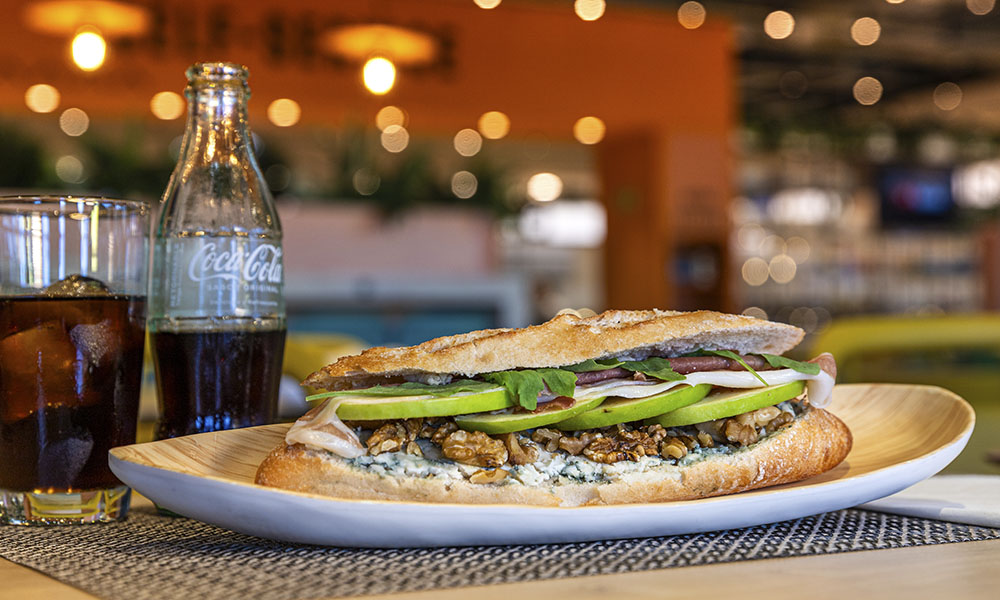 Bocadillo de queso azul con nueces, jamón y manzana Grand Smith junto a una Coca Cola realizado en un área de servicio