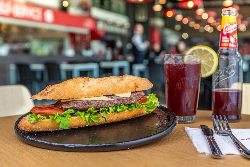 Bocadillo de carne vacuno con queso fundido, tomate y lechuga junto a tinto de verano