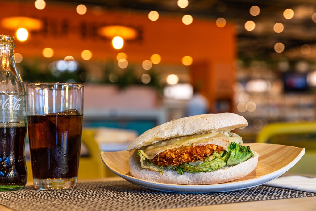 Bocadillo de pollo crujiente en pan de mollete con queso fundido y lechuga junto a refresco de Coca Cola