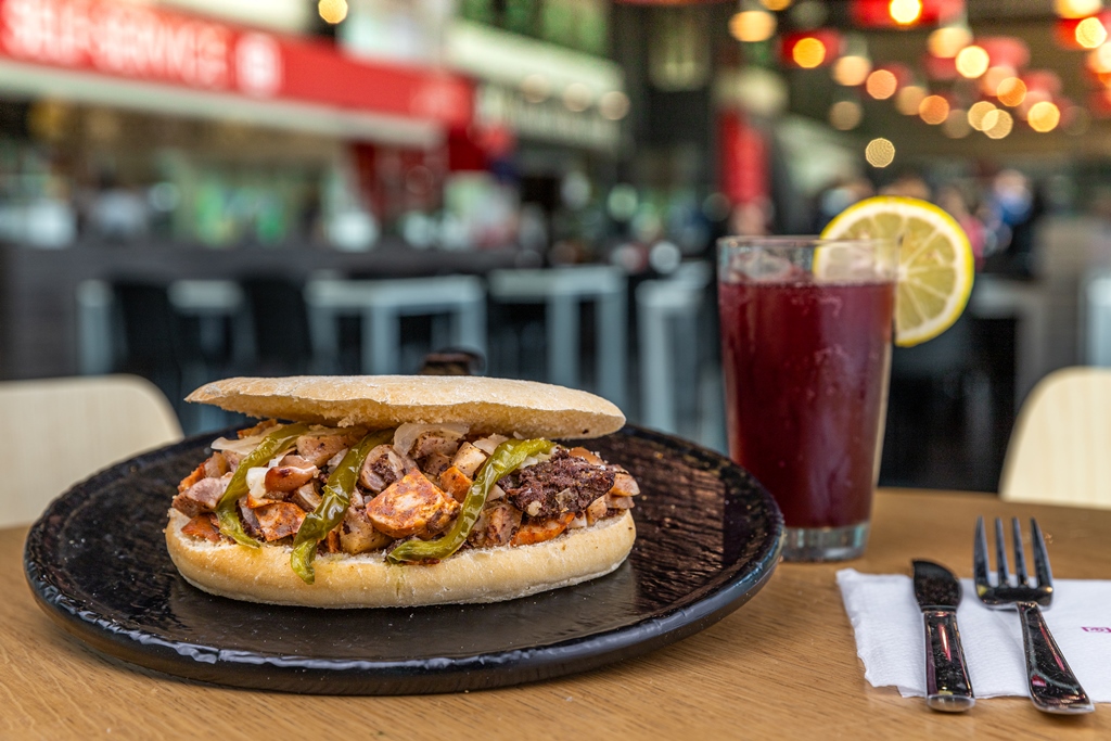 Mollete de pringa con cebolla caramelizada y pimientos verdes fritos junto a un tinto de verano